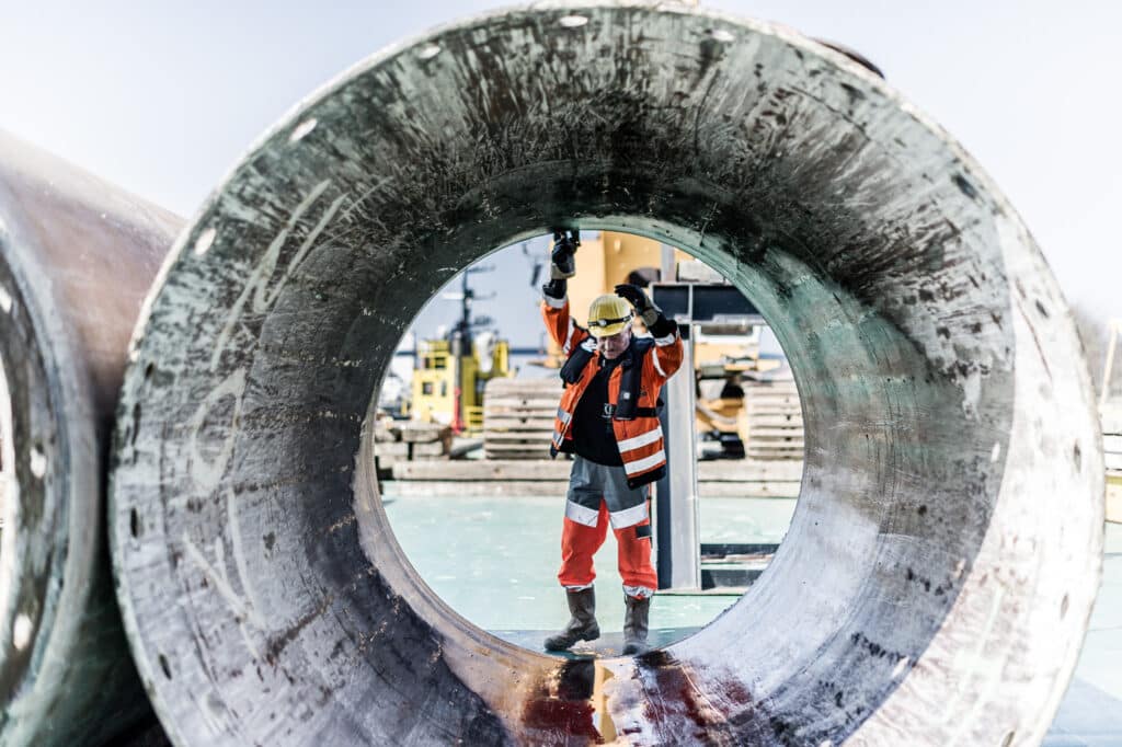 Arbeiter in Schutzkleidung mit großes Metallrohr auf einer Baustelle