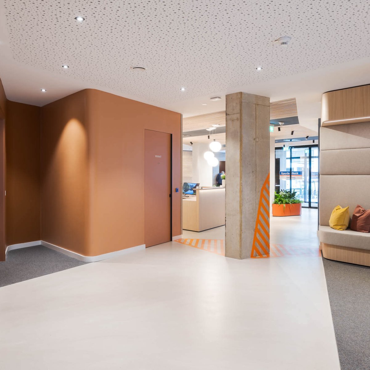Modernes Büro- oder Empfangsinterieur mit Sitznische, Betonstützen und warmen Wandfarben